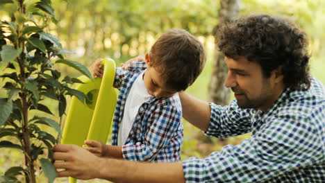Portrait-of-a-boy-and-his-dad-watering-a-tree.-Dad-helps-his-son.-Happy-family.-Blurred-background